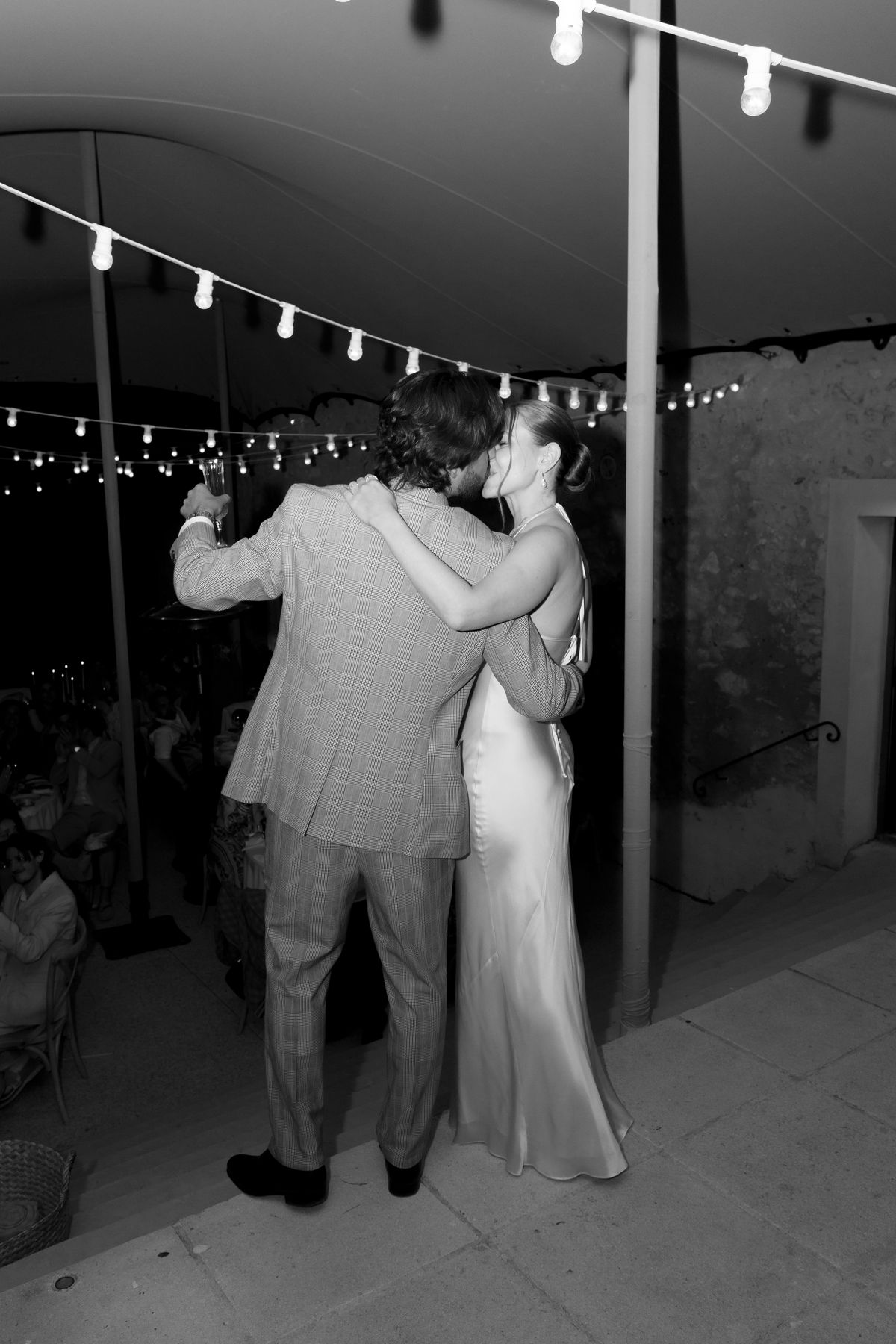 Bride and groom slow dancing under string lights at night, black and white