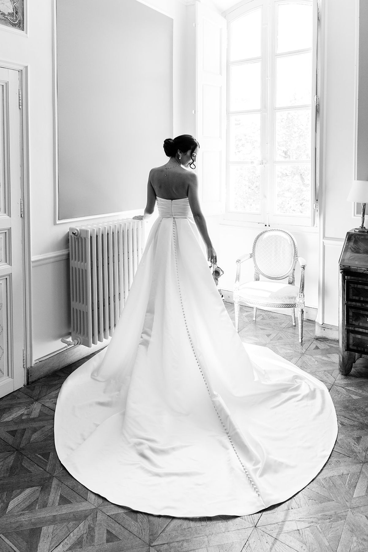 Bride from behind in a strapless gown with a long train across a parquet floor, black and white