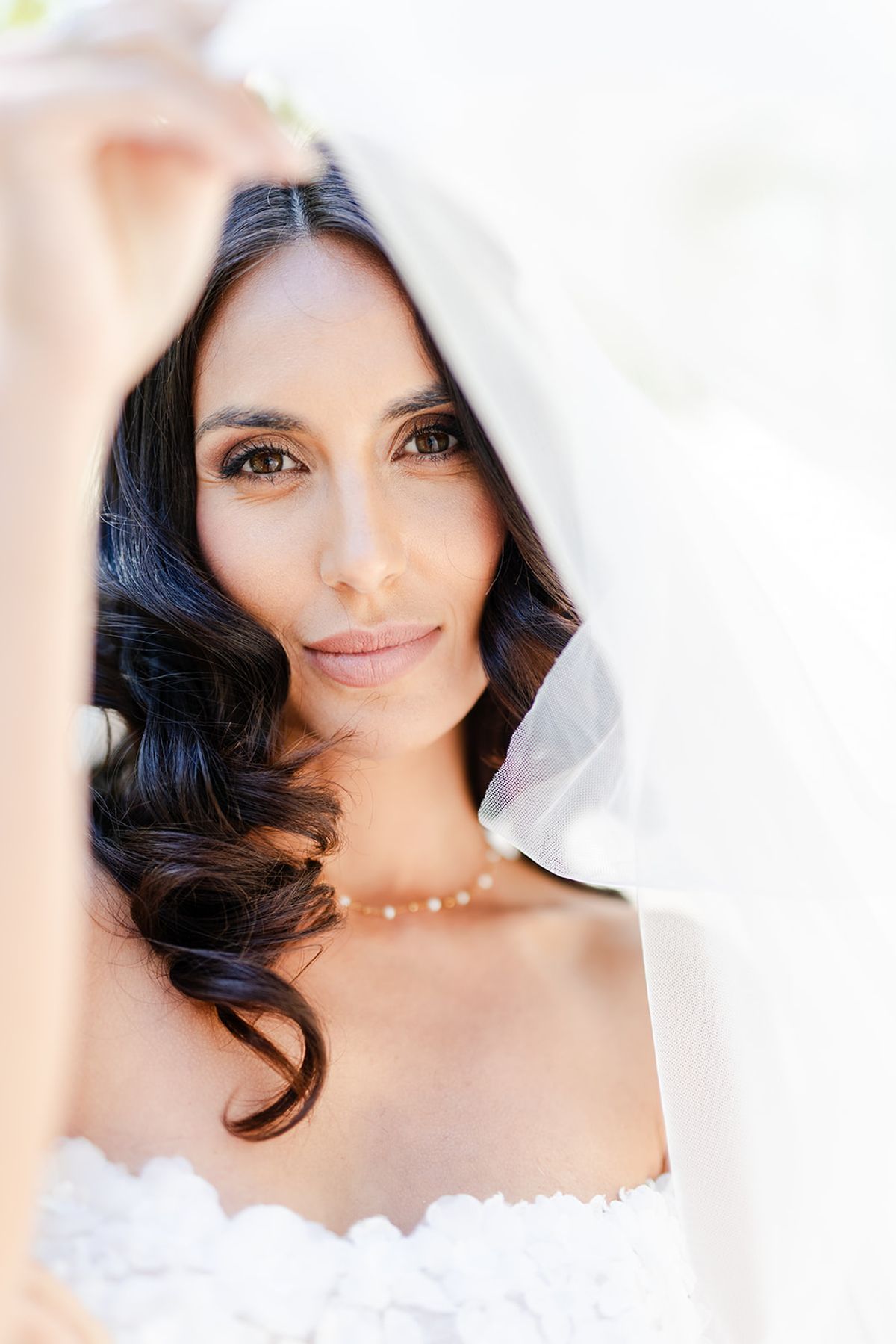 Close portrait of the bride framed by her tulle veil, wearing a pearl necklace