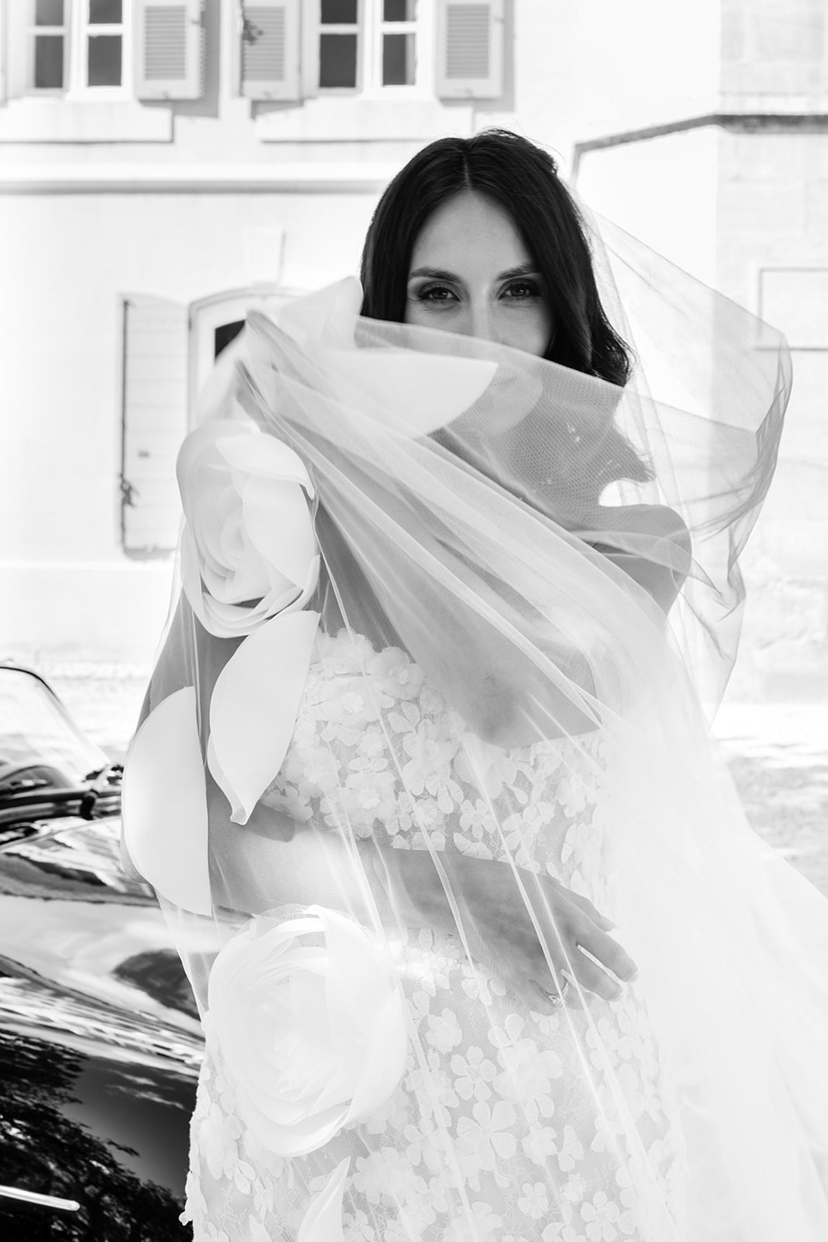 Bride lifting her veil beside the vintage car, black and white