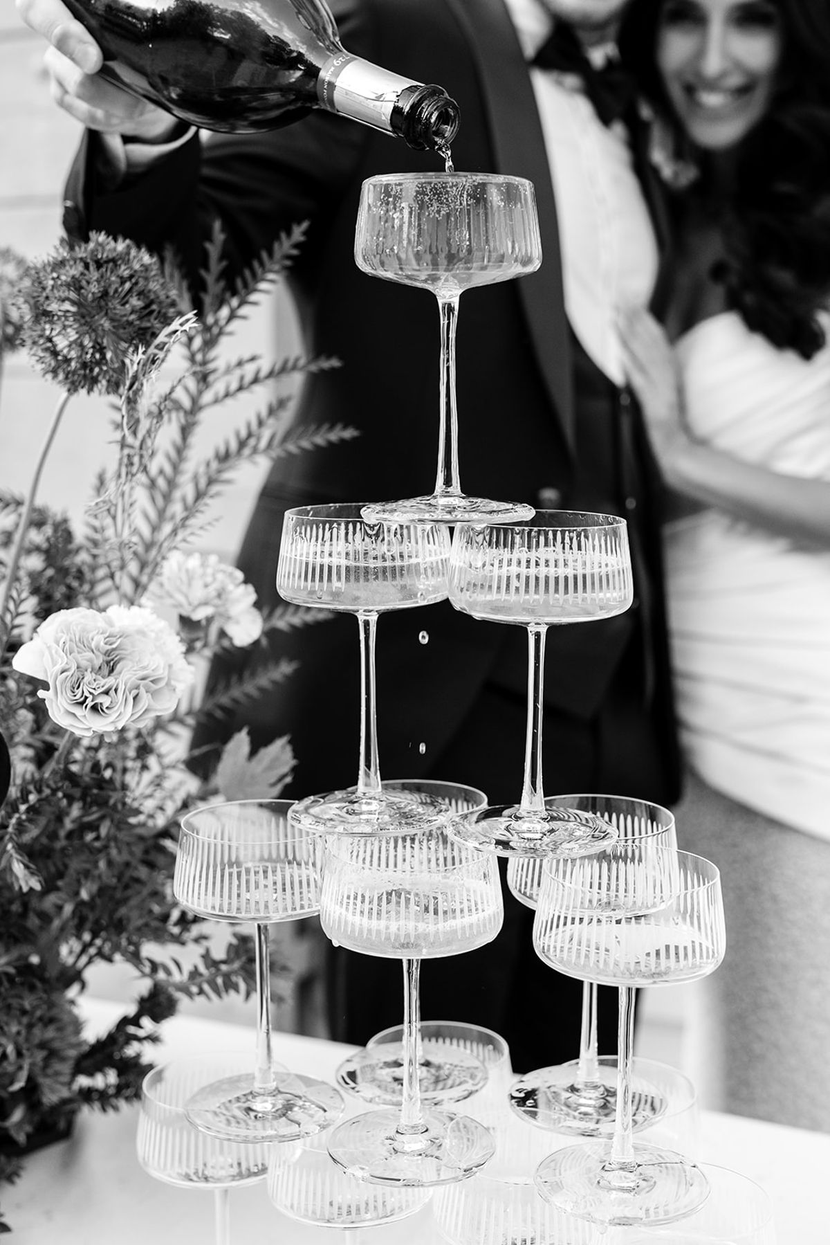 Champagne being poured into a tower of ribbed coupes, black and white