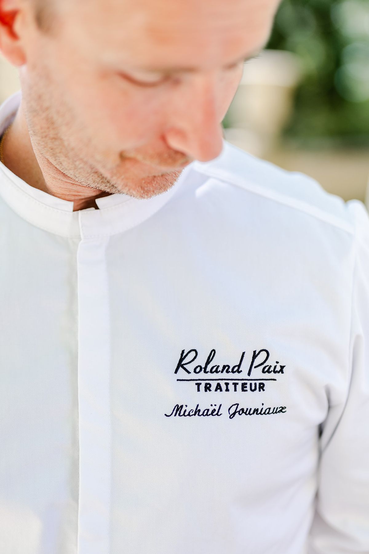 Chef looking down in a white jacket embroidered Roland Paix Traiteur