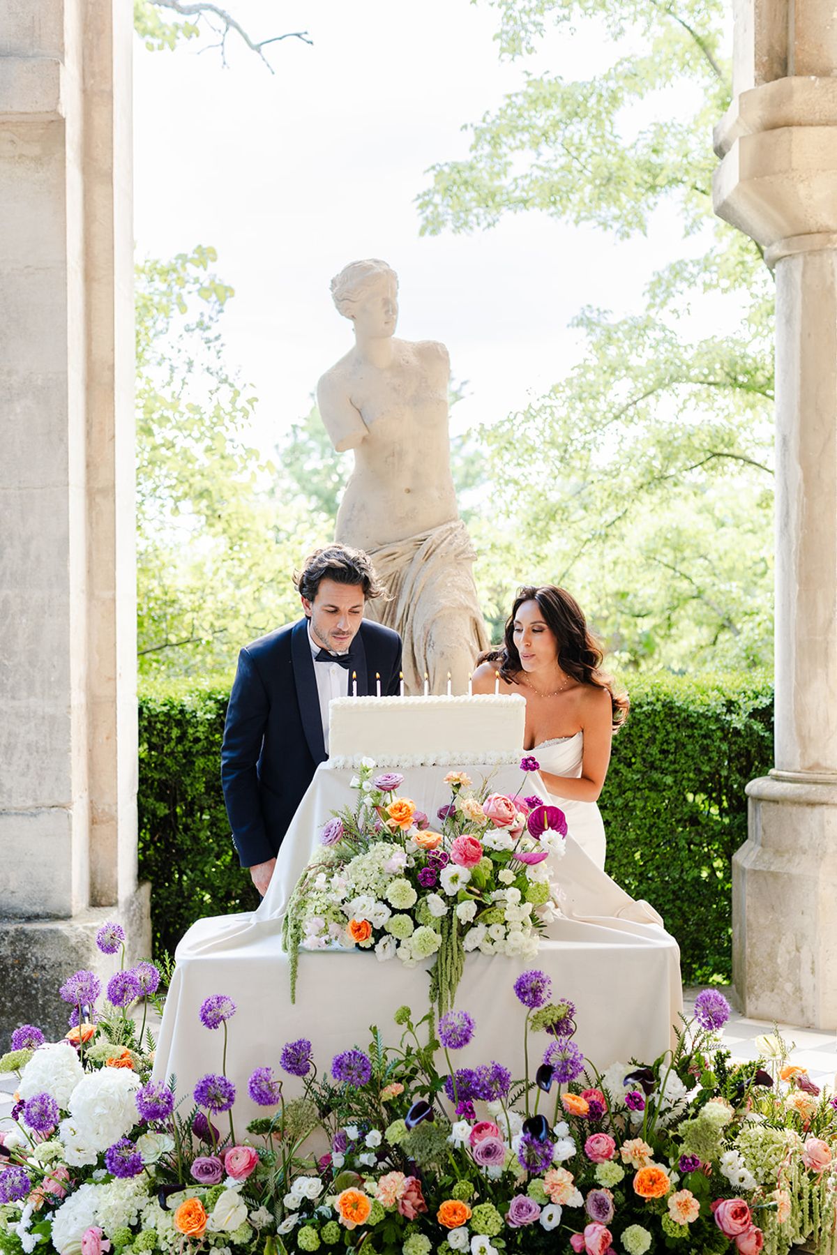 Couple blowing out the candles on a white cake between the stone columns of the loggia