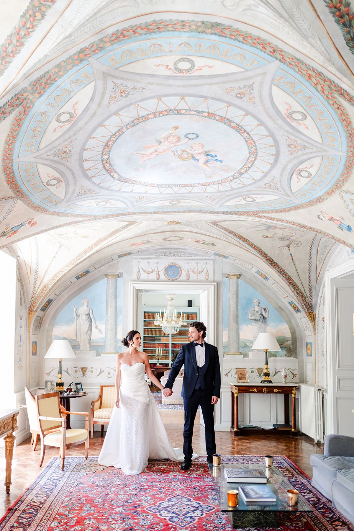 Couple holding hands under the painted vaulted ceiling of a salon at Château de Pradines