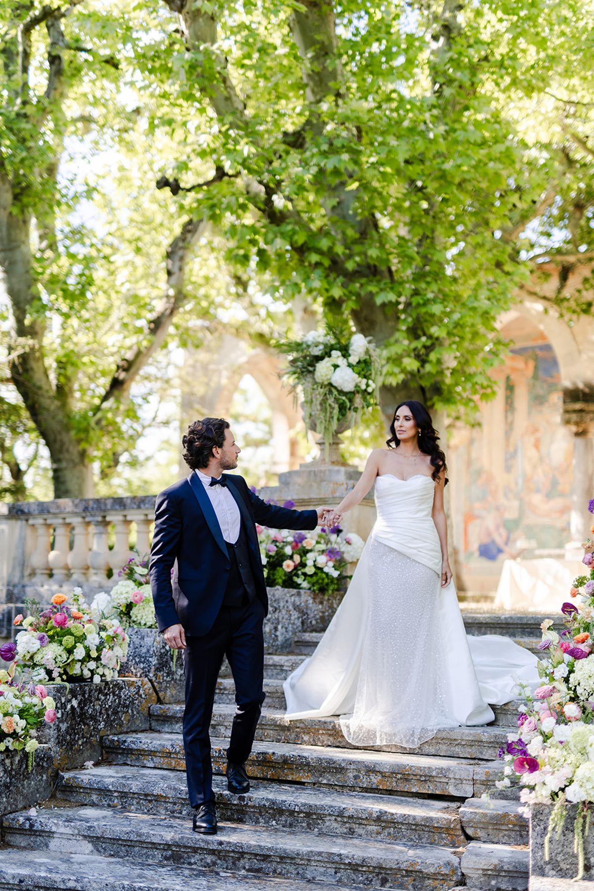 Groom leading the bride down a stone staircase lined with colourful flowers