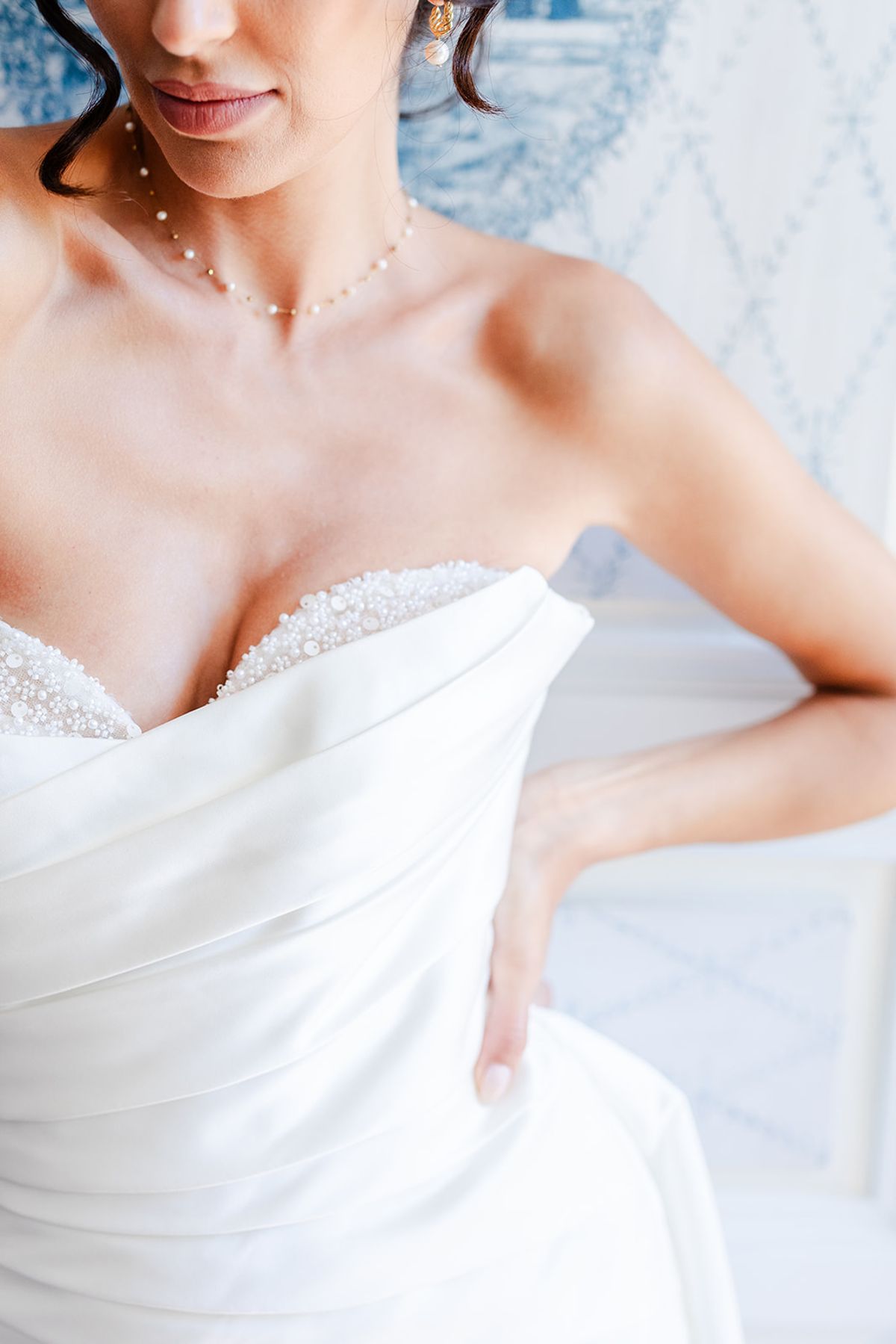 Close detail of a draped strapless satin bodice with a pearl necklace