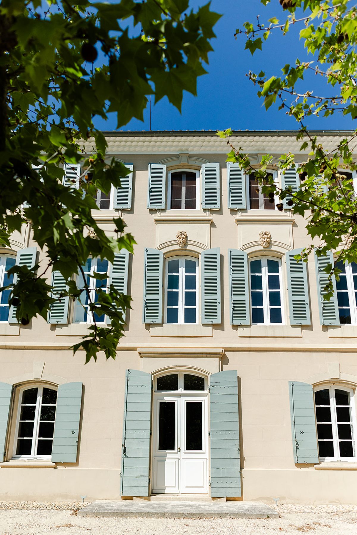 Château de Pradines façade with blue-grey shutters framed by plane tree leaves