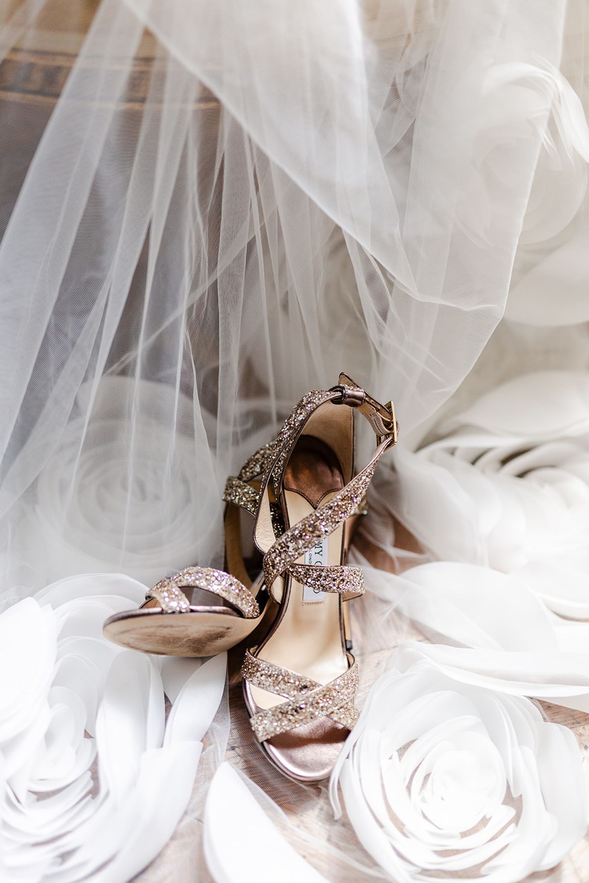 Glitter strappy heels resting on a tulle veil and white fabric roses