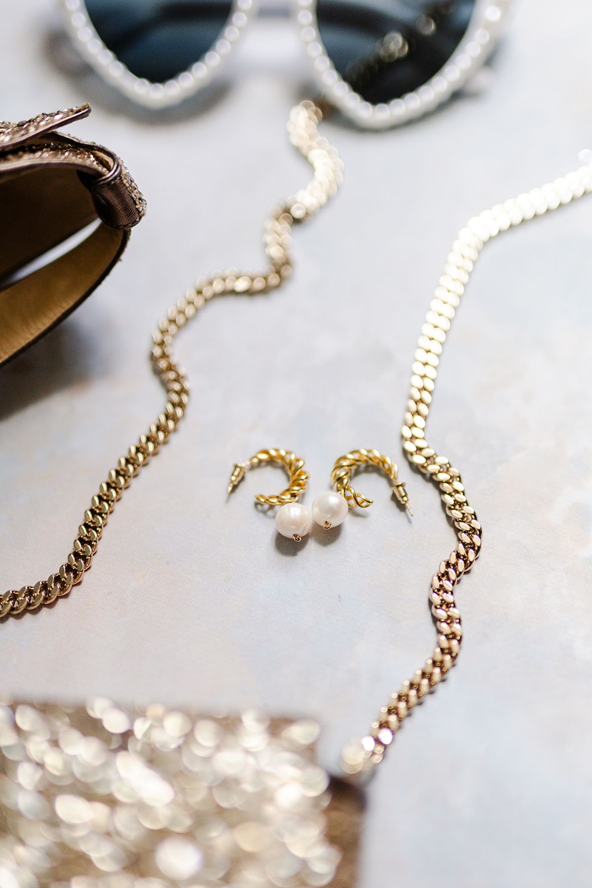 Gold chain necklace, pearl hoop earrings and pearl-trimmed sunglasses laid out for the bride