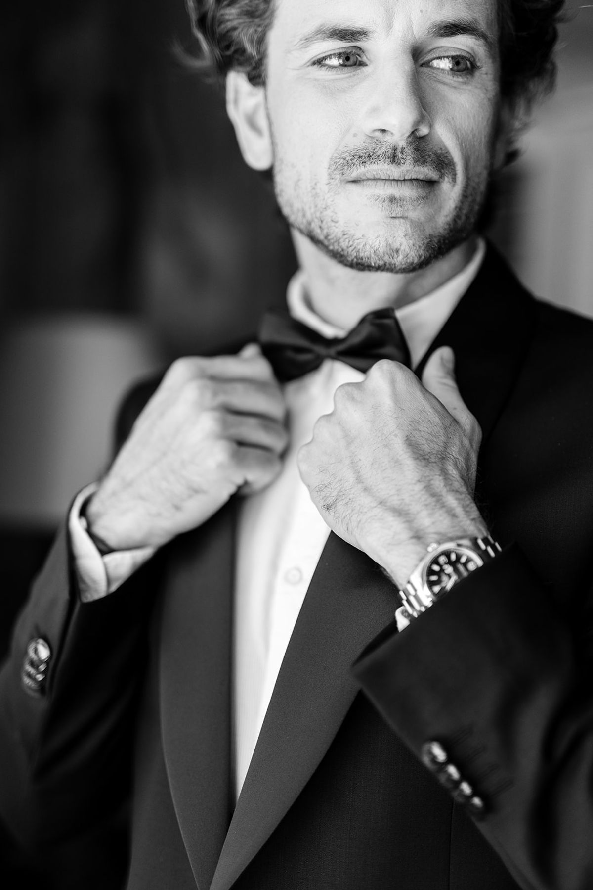 Groom adjusting his bow tie in a dark tuxedo, black and white