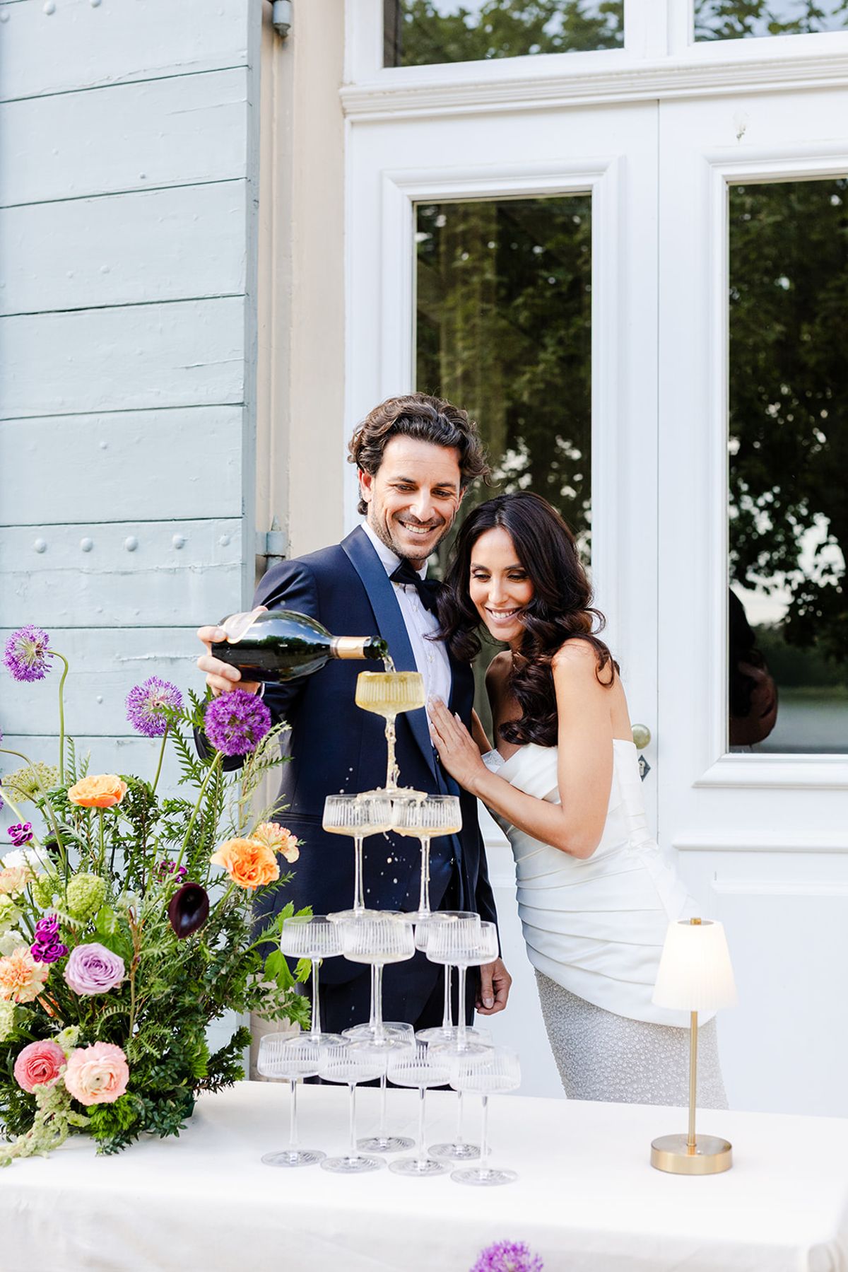 Groom pouring champagne into a coupe tower with the bride at his side