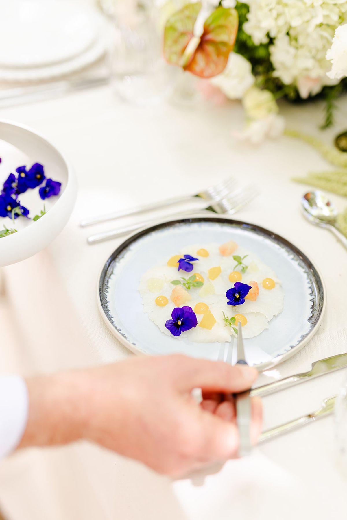 Hand lifting cutlery over a plated starter with edible violas