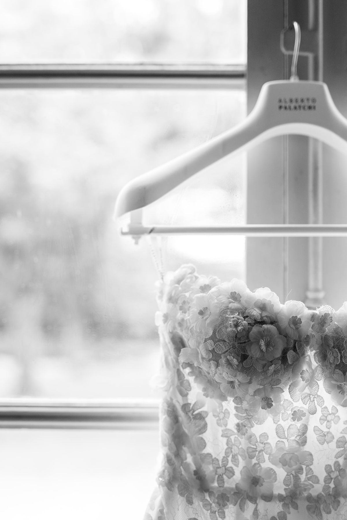 Black and white detail of a floral lace bodice on a hanger by a window