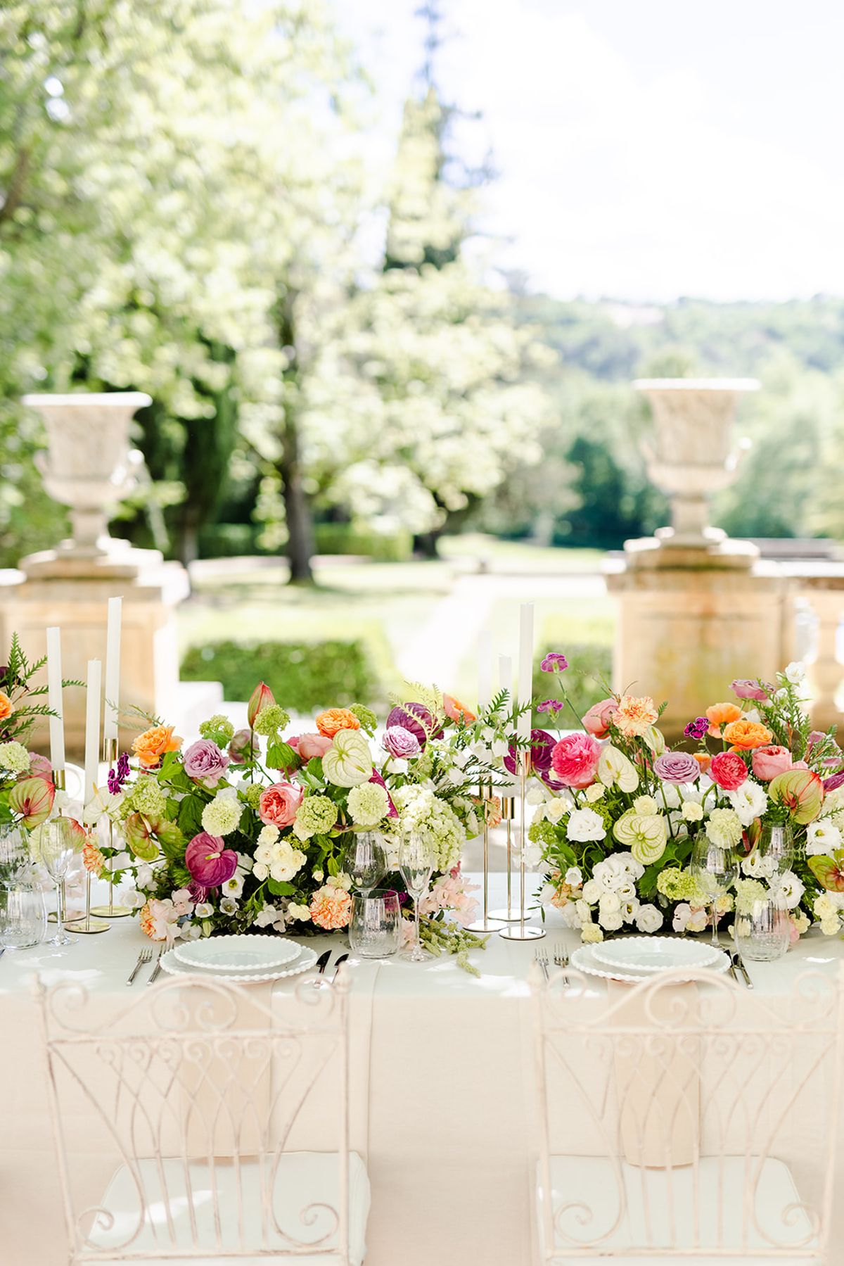 Long dinner table with low colourful flowers on the terrace between stone urns