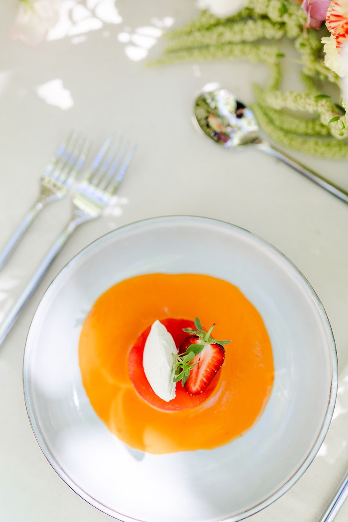 Bowl of orange melon soup with strawberry and cream, seen from above