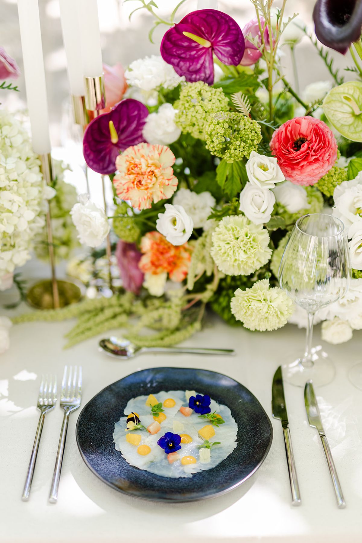 Place setting with a dark plate beneath an arrangement of anthurium, roses and hydrangea