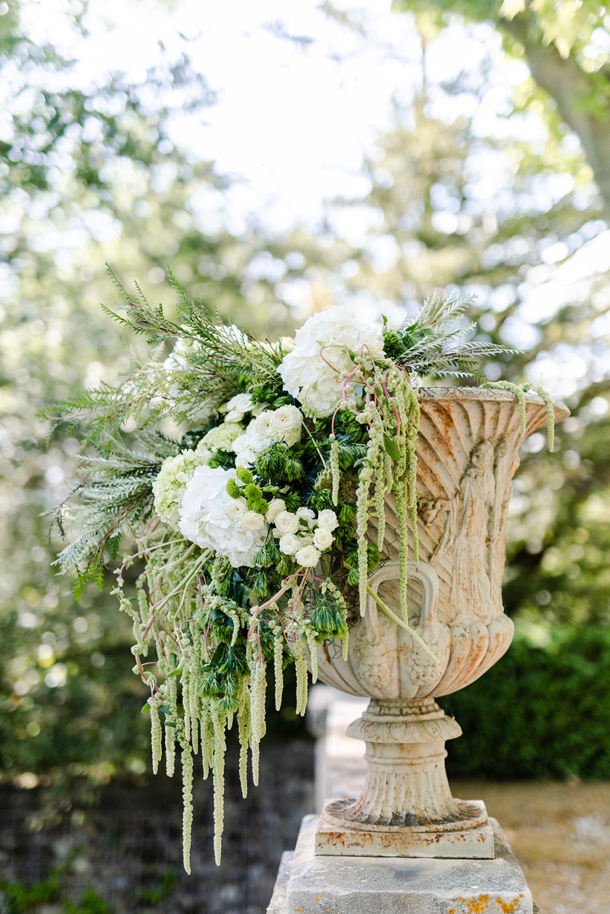 Stone urn filled with white flowers and trailing green amaranthus in the gardens
