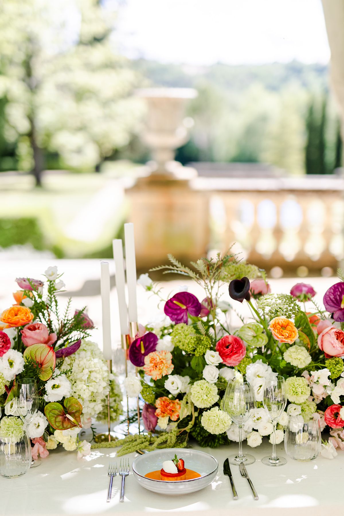 Low floral arrangement with white taper candles beside a plated course