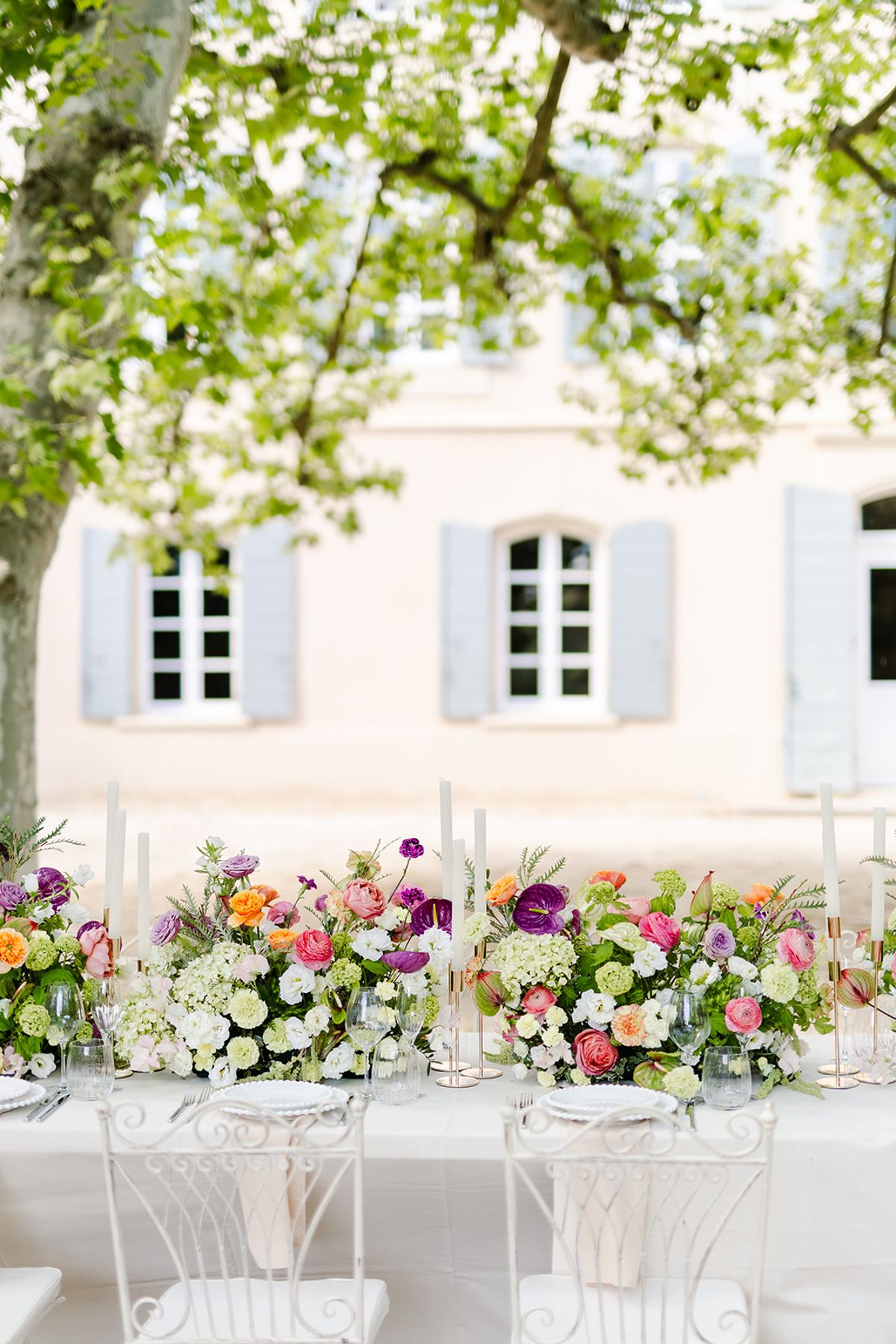 White garden chairs and flowers along the table in front of the château shutters