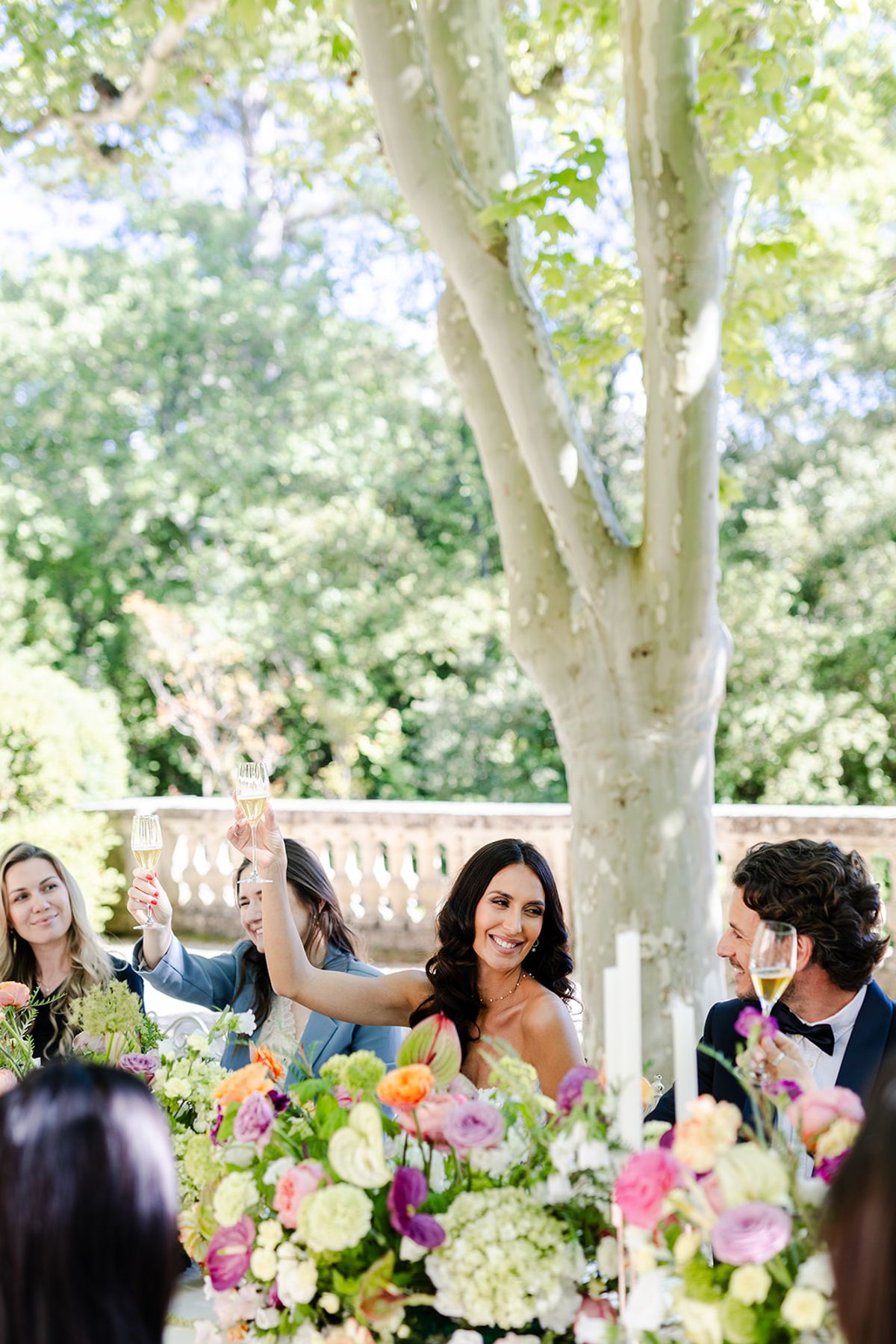 Bride raising a glass with others around the flower-filled dinner table