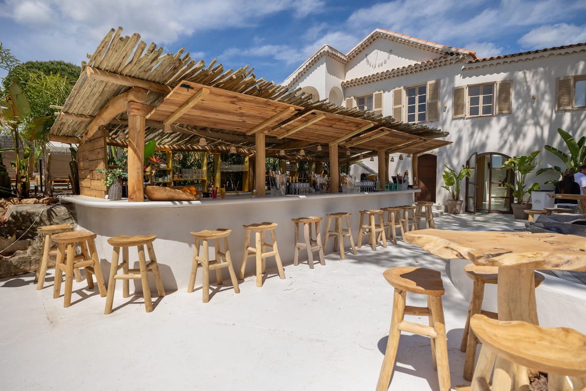 Long tables set for a wedding dinner on the terrace beneath the pergola and string lights
