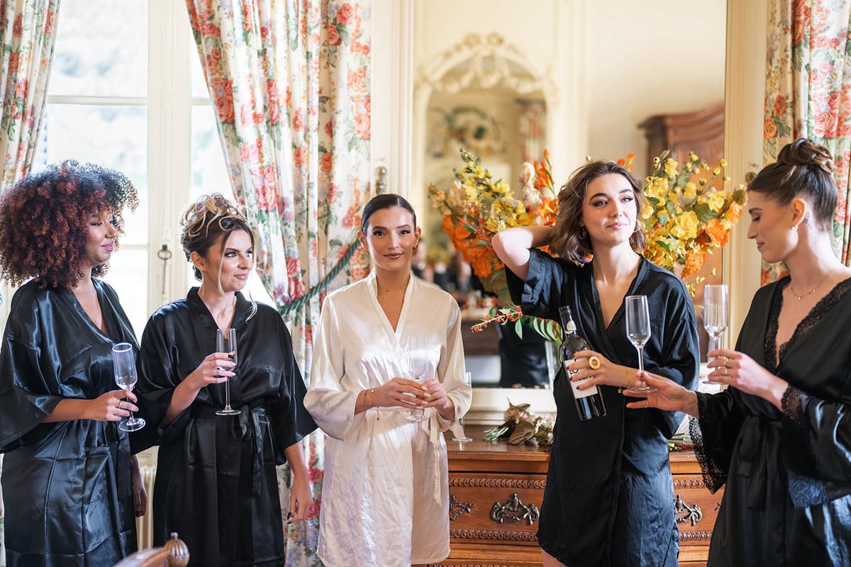Five women in robes with champagne before a mirror and autumn flowers in Château du Terral's Claude suite