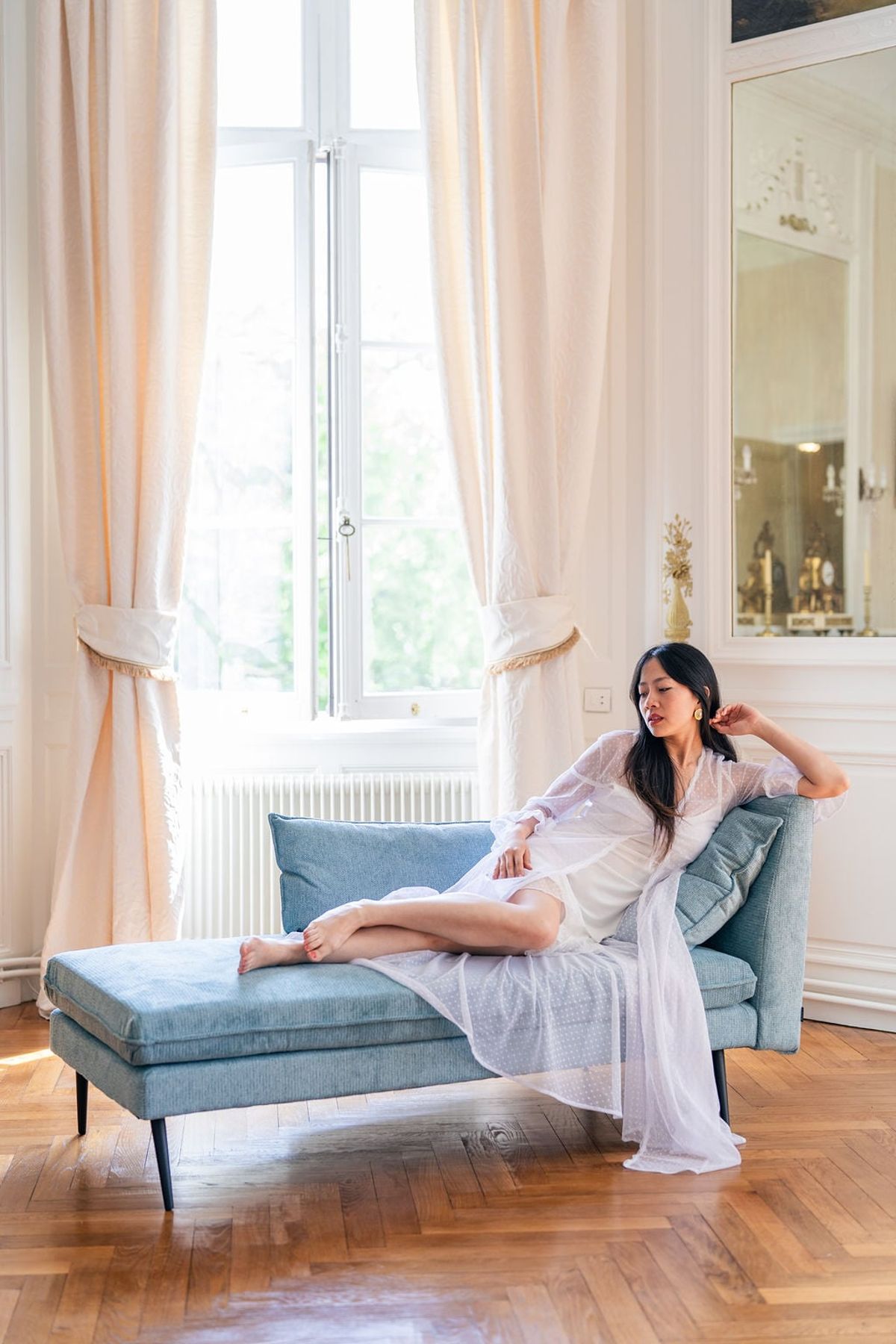 Bride reclining on a blue daybed by a sunlit window in a Château du Terral suite