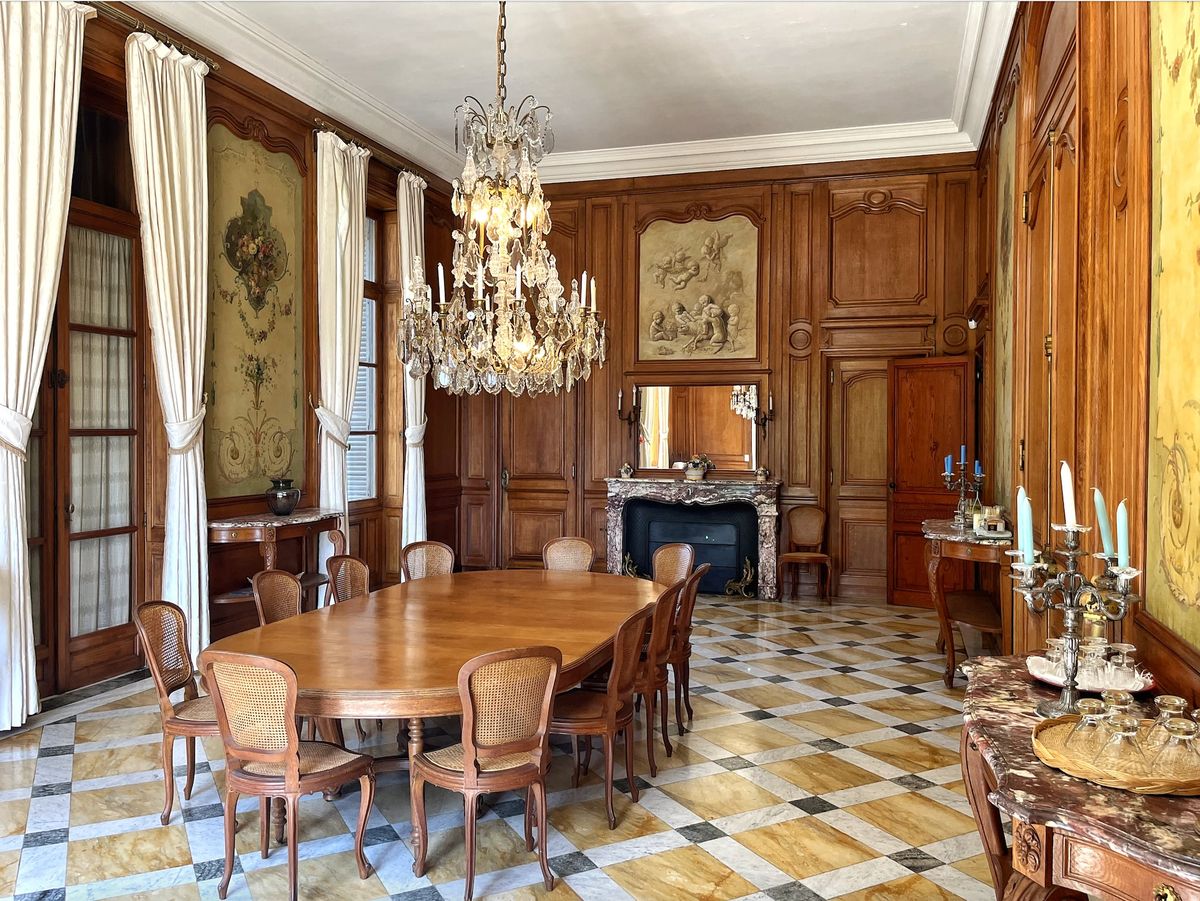 Wood-panelled dining room at Château du Terral with long table, chandelier and marble fireplace