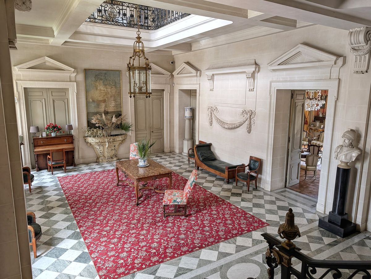 Château du Terral entrance hall with chequered floor, red floral rug, brass lantern and antique furnishings