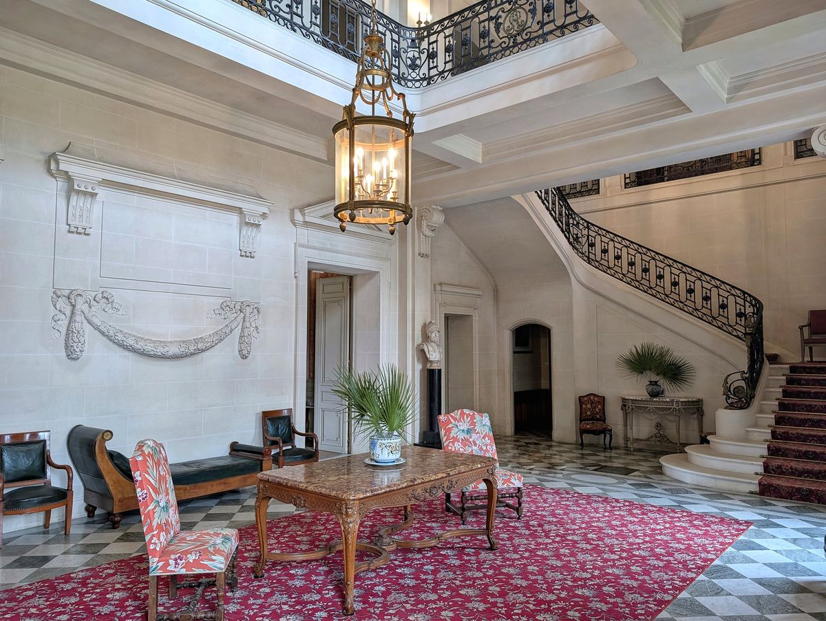 Grand stone entrance hall at Château du Terral with sweeping staircase, brass lantern and red patterned rug