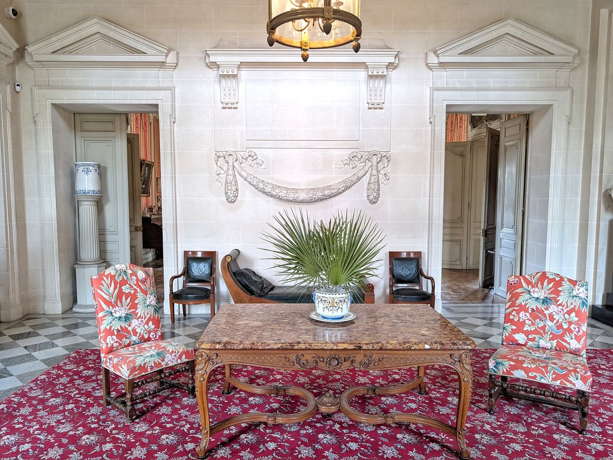 Château du Terral hall with marble-top table, coral floral armchairs, potted palm and carved stone garland
