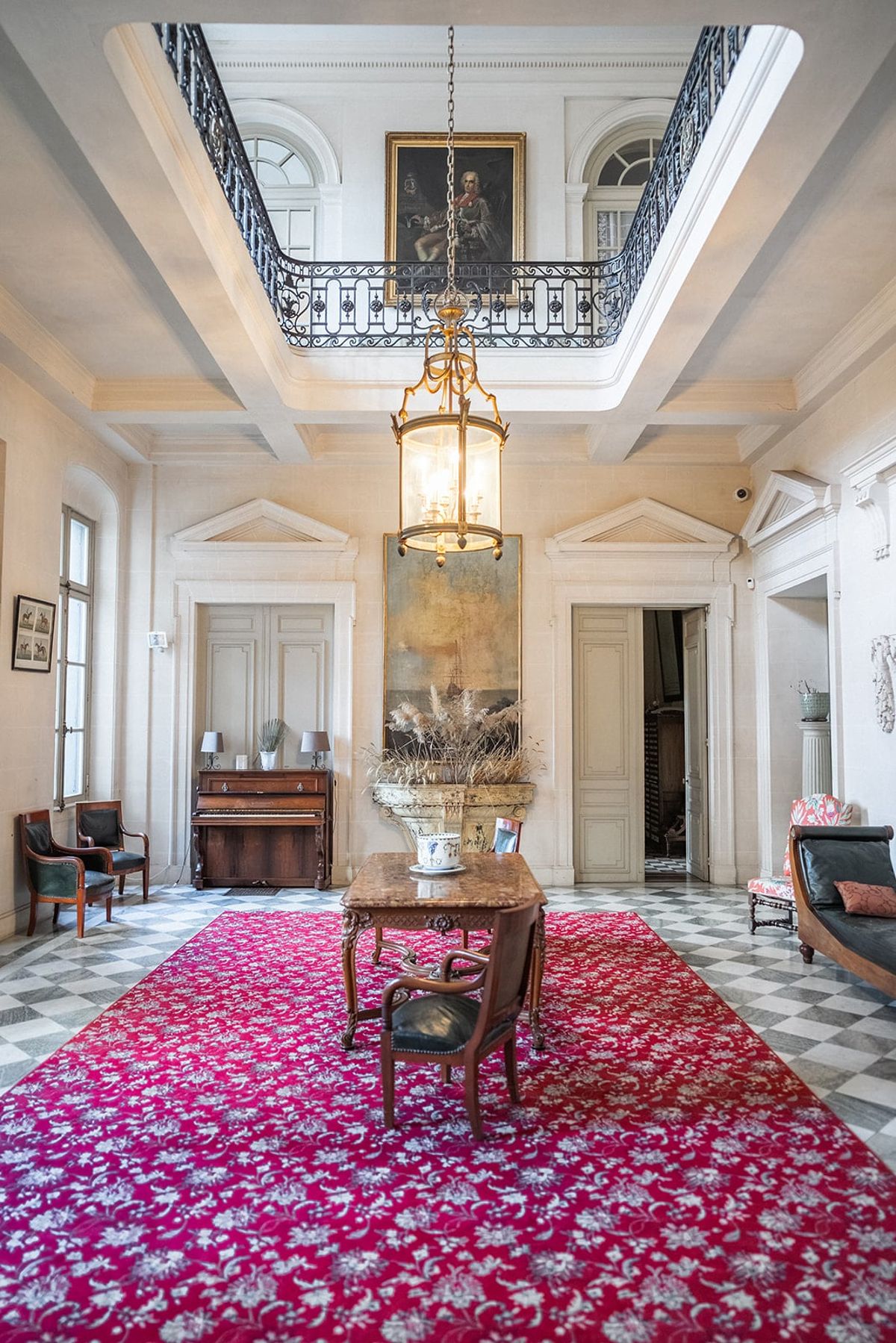 Soaring entrance hall at Château du Terral with portrait, chandelier-lantern and crimson floral carpet