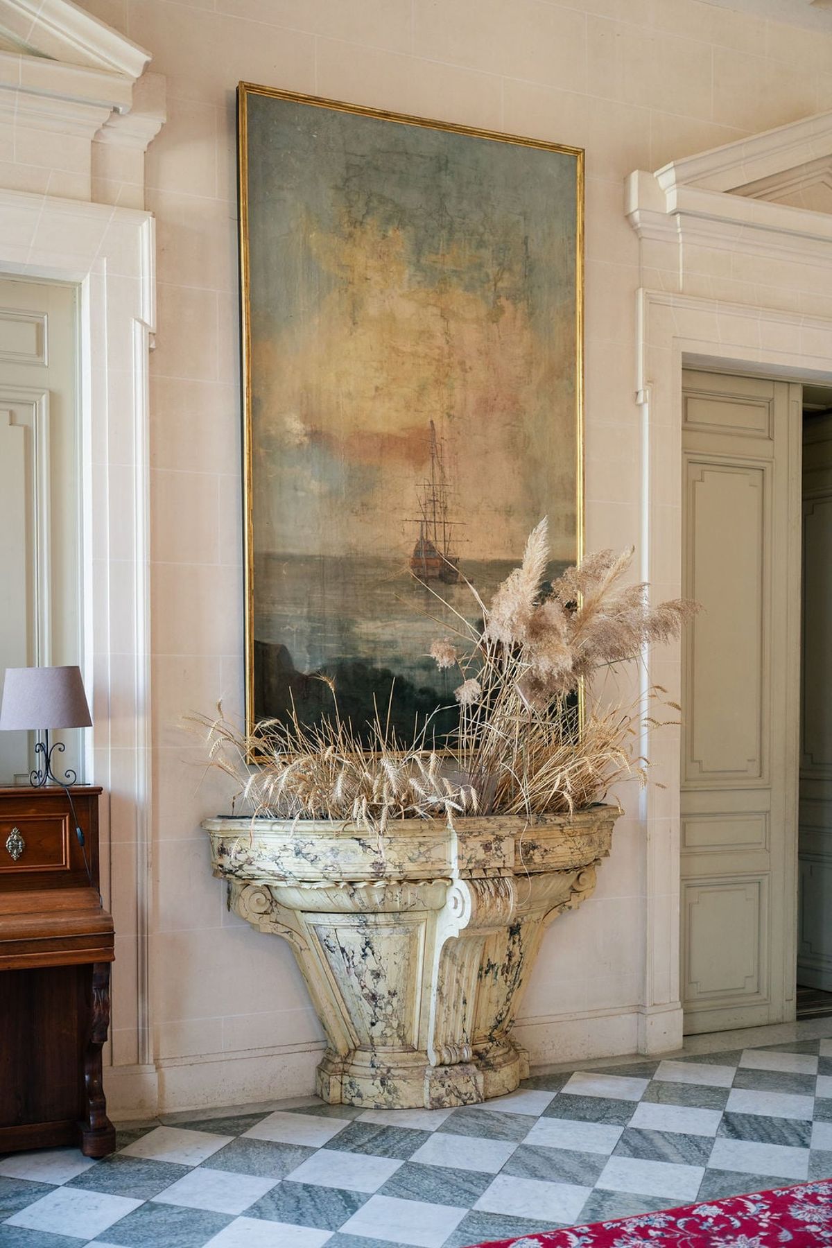 Marble urn of dried pampas below a seascape painting on the chequered entrance hall floor at Château du Terral