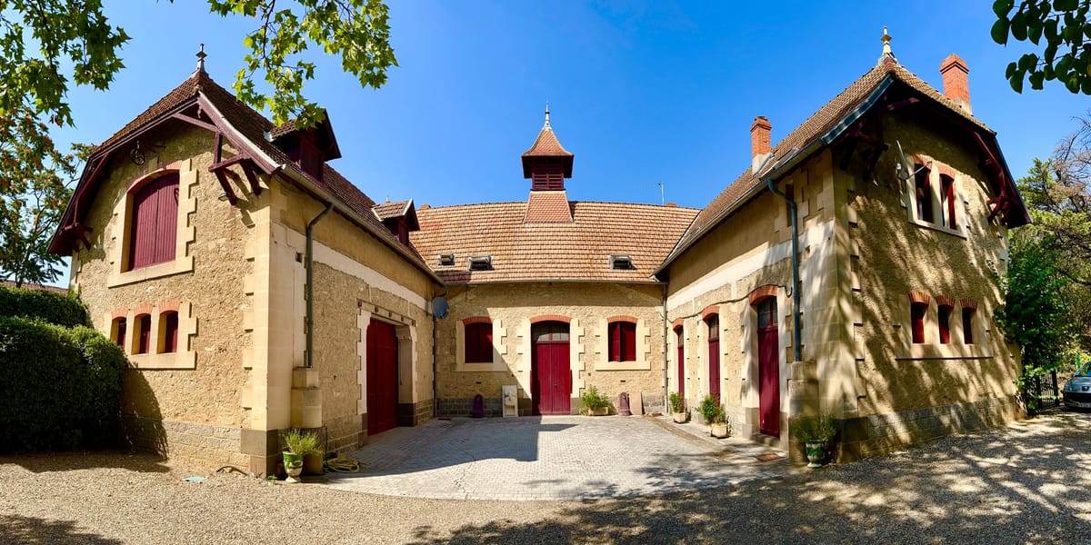 Stone outbuildings with red doors and tiled turret around the courtyard at Château du Terral