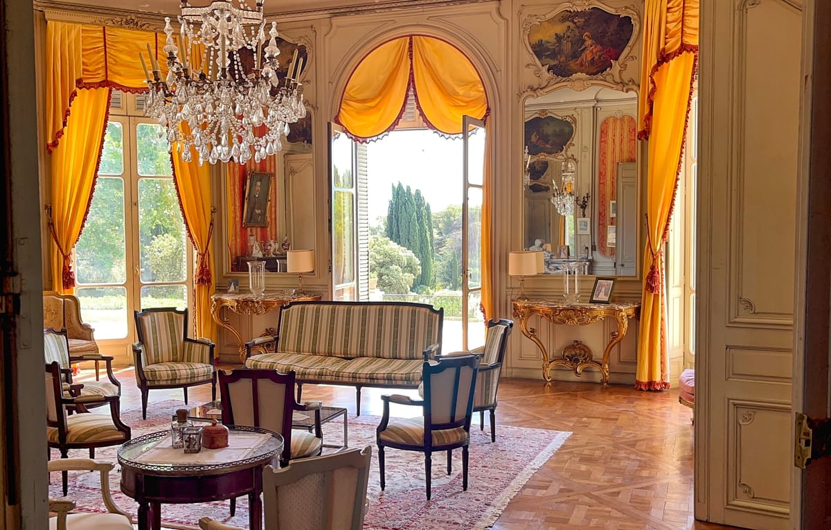 Grand salon at Château du Terral with crystal chandelier, gold drapes and antique seating by garden windows