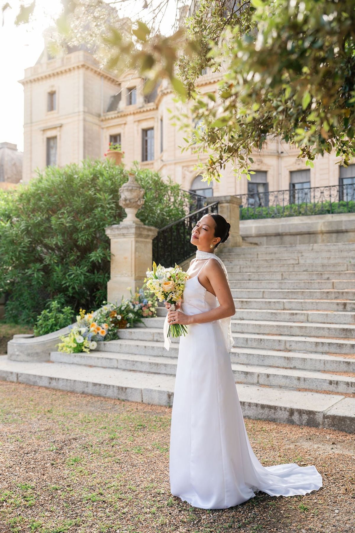 Bride with a yellow bouquet on the stone garden steps of Château du Terral in golden light