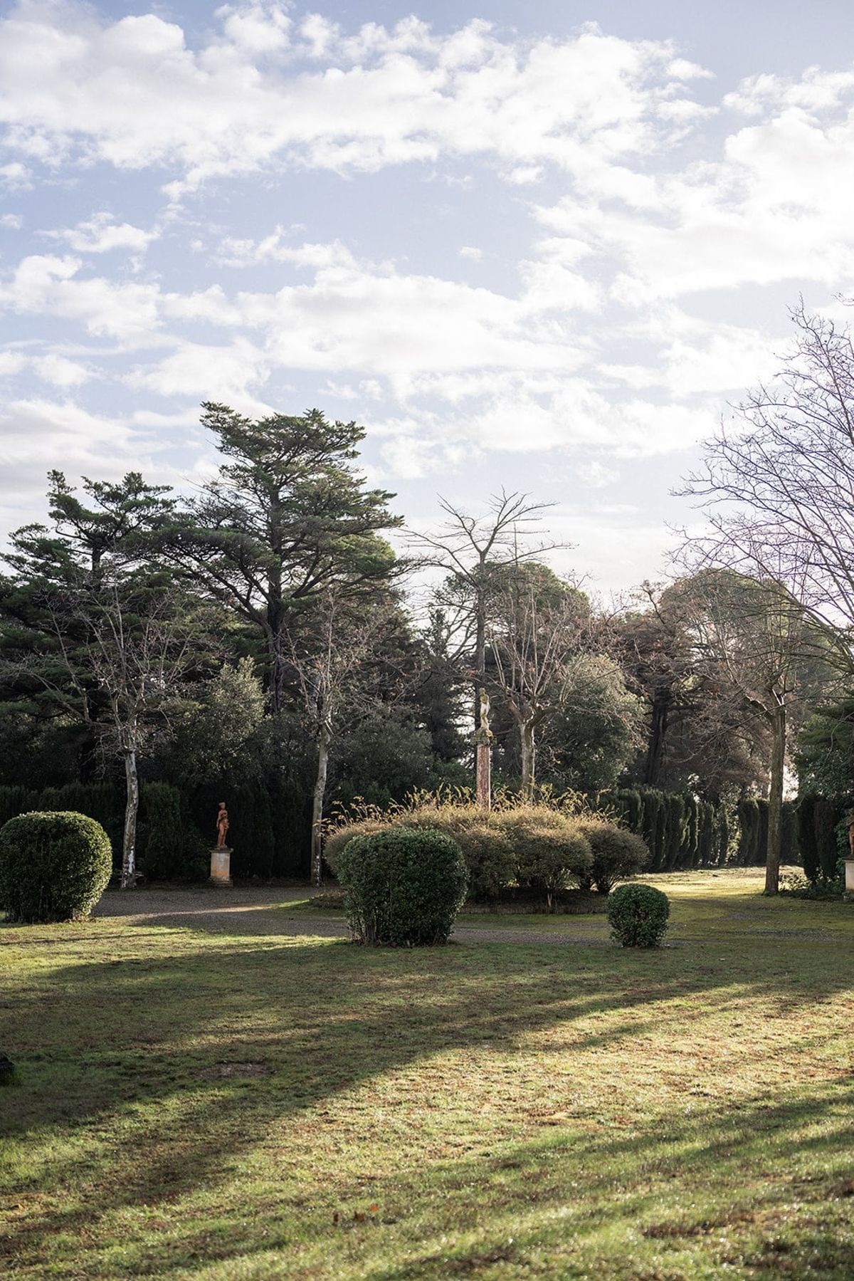 Lawns, clipped topiary and a garden statue among mature trees in the grounds of Château du Terral