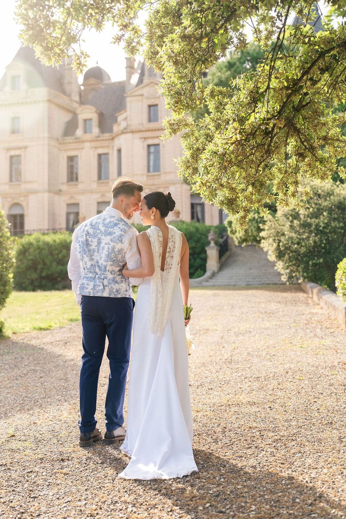 Couple sharing a moment on a tree-lined gravel path with Château du Terral behind in evening light