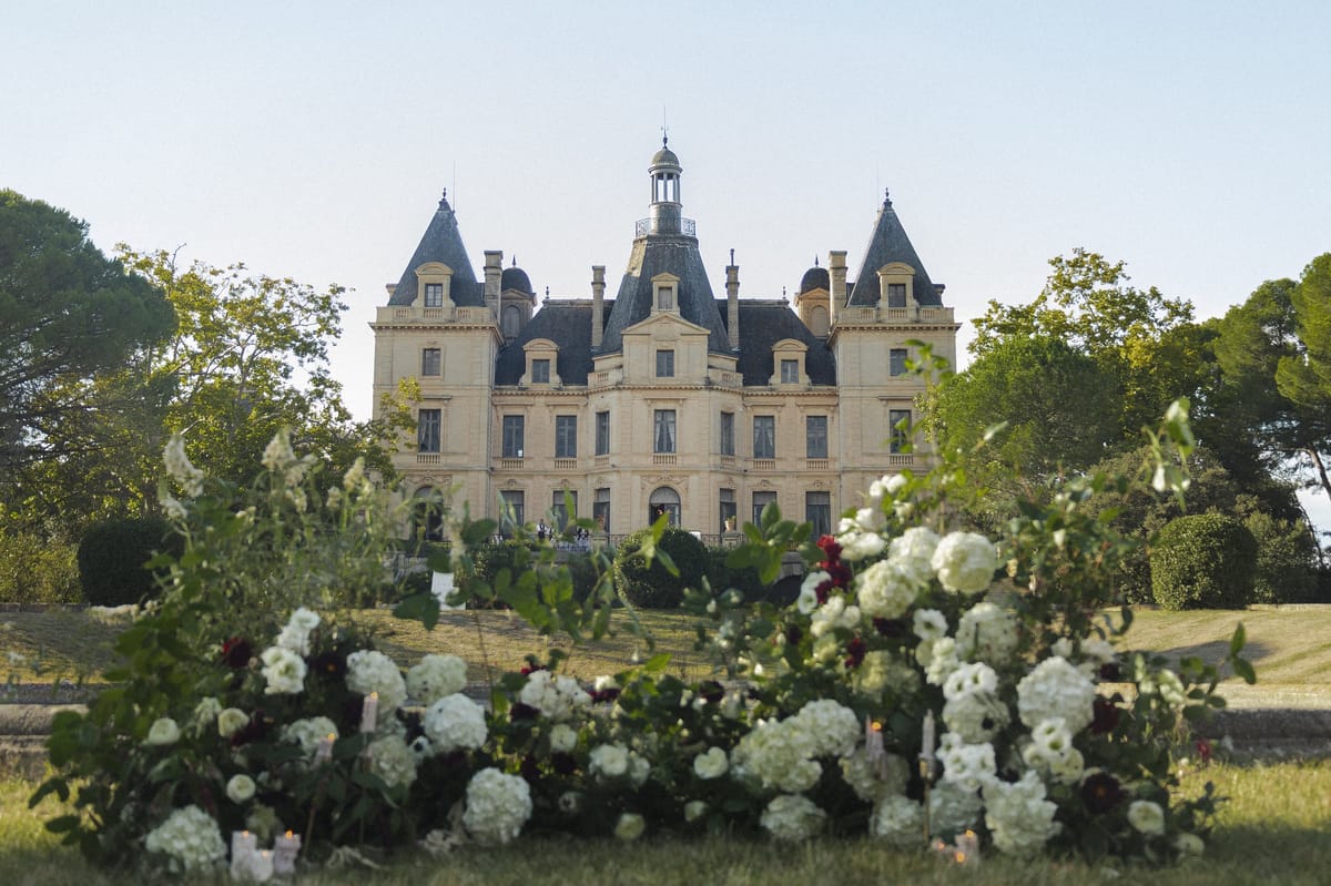 Château du Terral's turreted facade framed by trees above a foreground of white and burgundy blooms