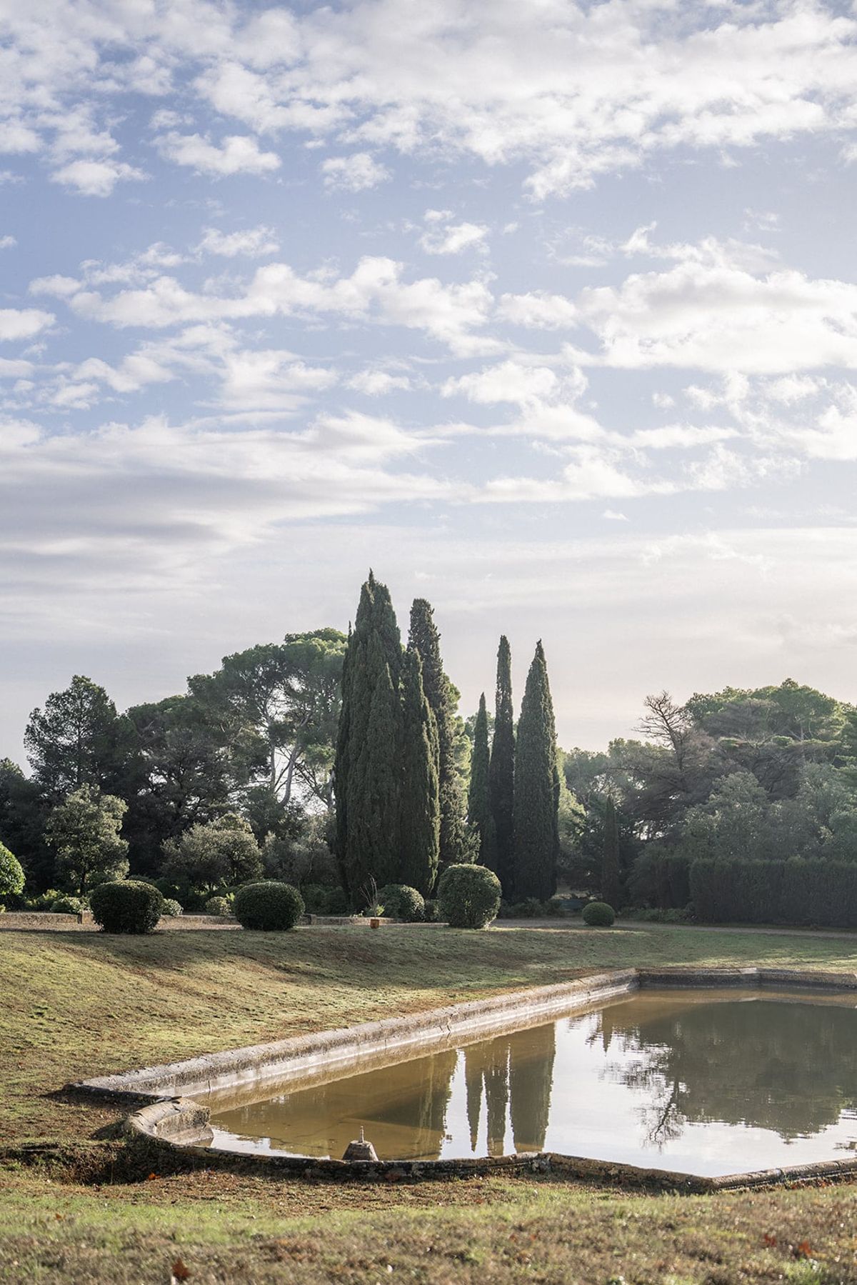 Tall cypress trees and an ornamental pond in the parkland grounds of Château du Terral