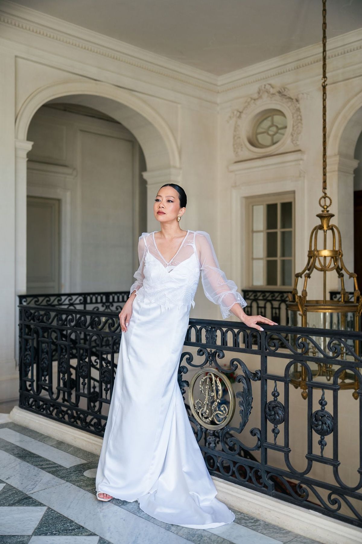 Bride in a sheer-sleeved gown on Château du Terral's landing beside ornate wrought-iron balustrade