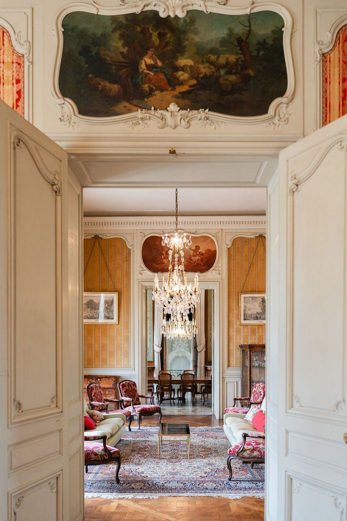 View through doorways into Château du Terral's salon with painted ceiling, chandelier and antique seating