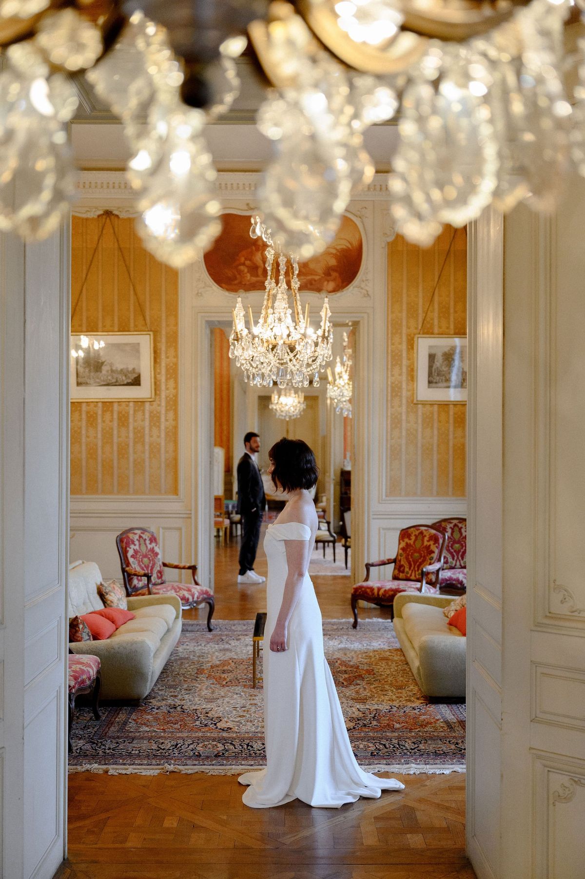 Bride before a crystal chandelier in Château du Terral's yellow-panelled salon with antique sofas