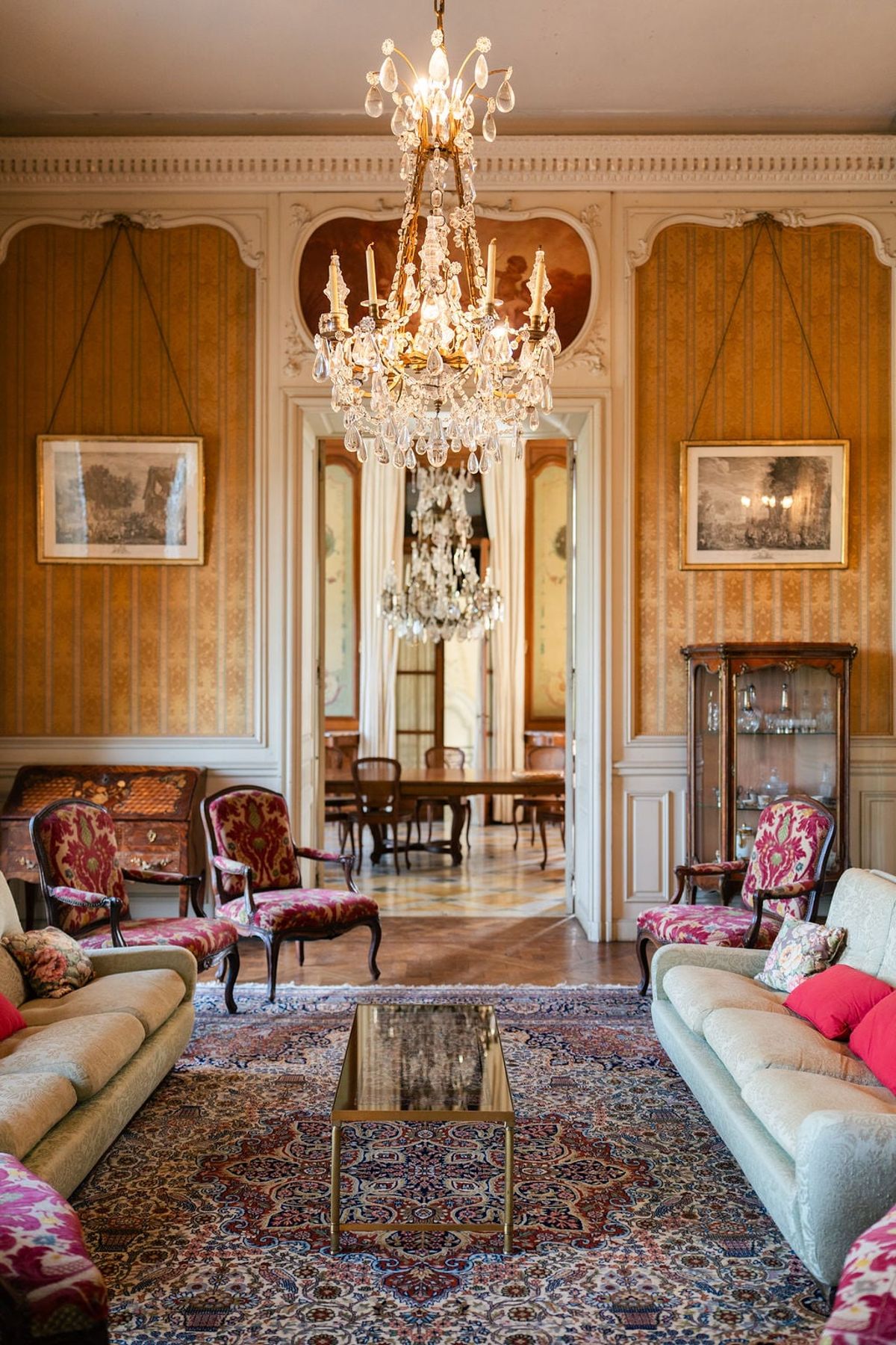 Drawing room at Château du Terral with crystal chandelier, upholstered sofas, framed prints and a rug