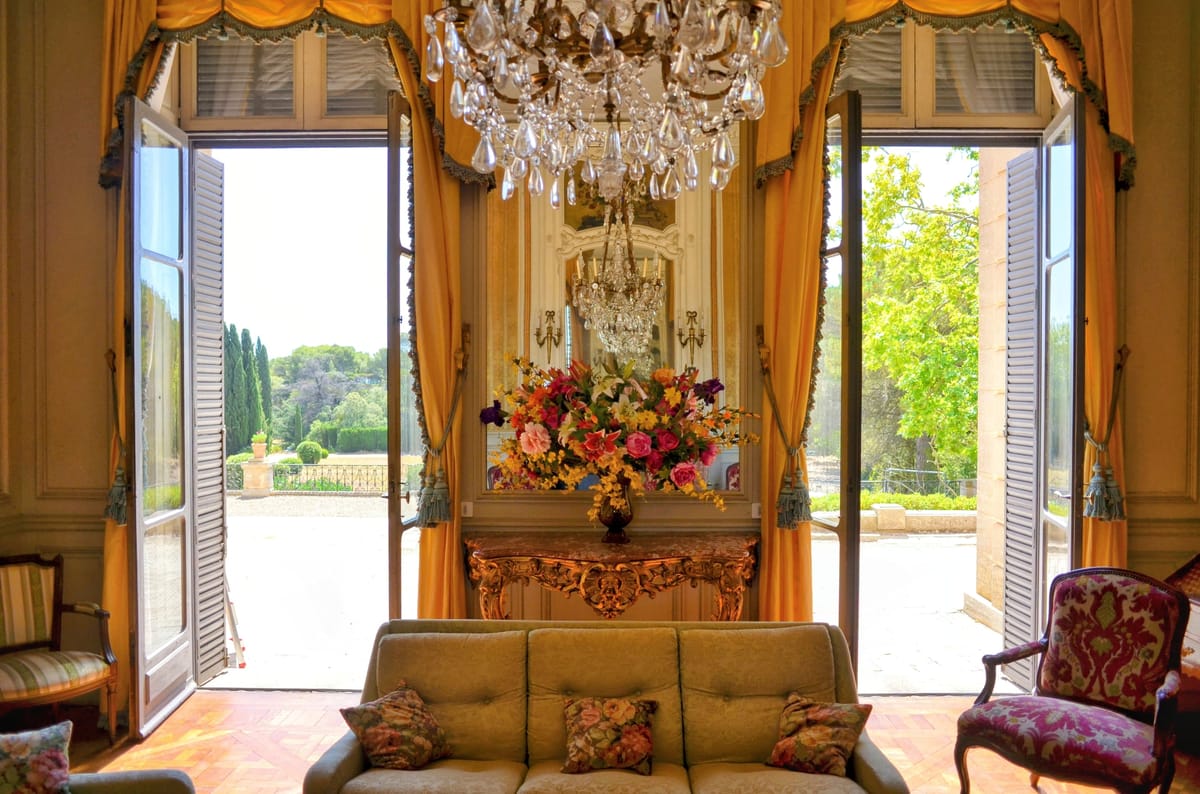 Open French doors at Château du Terral framing the gardens, with a gilt console and flowers