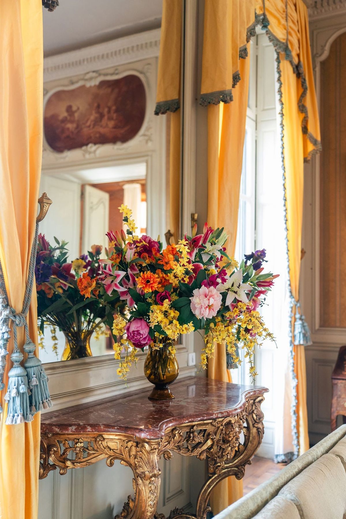 Colourful floral arrangement on a marble-topped gilt console beneath a mirror at Château du Terral
