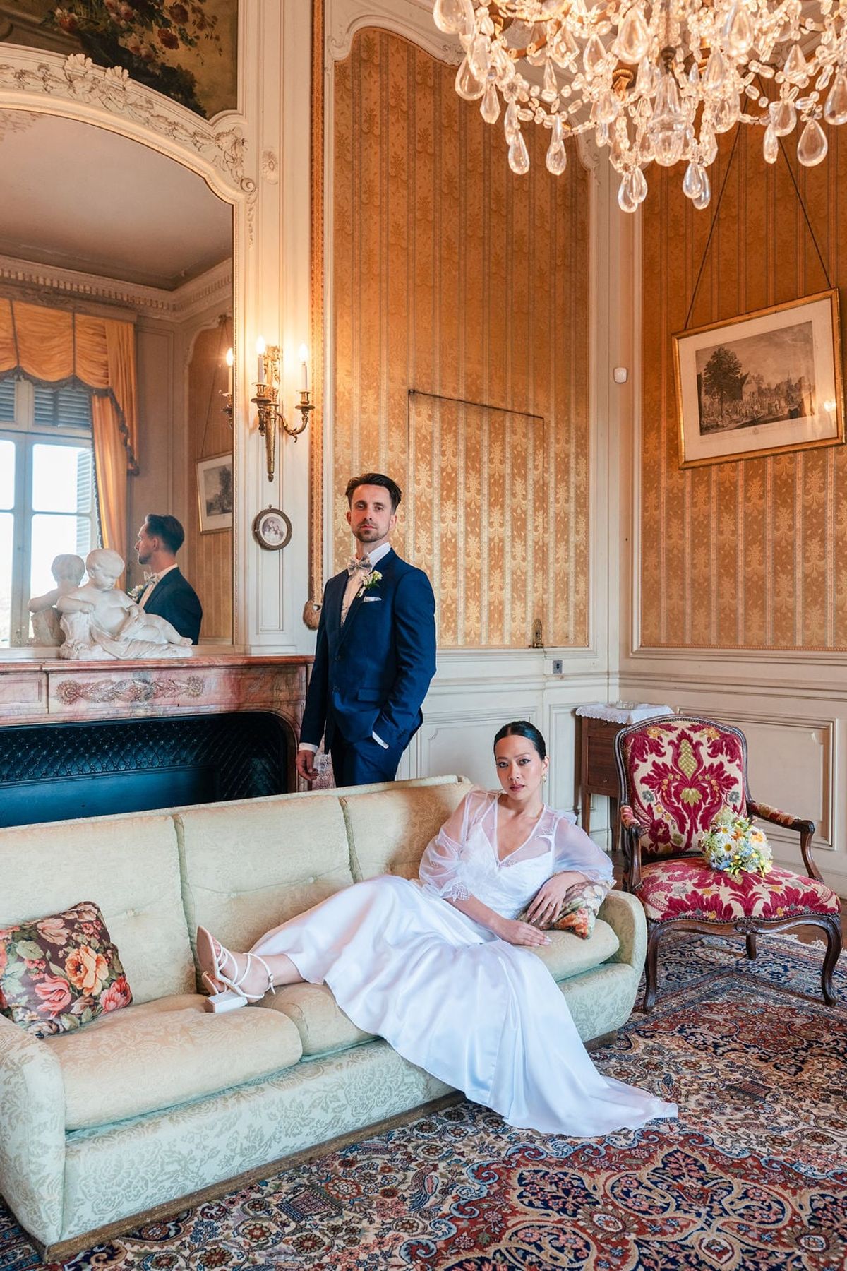 Bride and groom in a Château du Terral salon with chandelier, fireplace and damask chairs