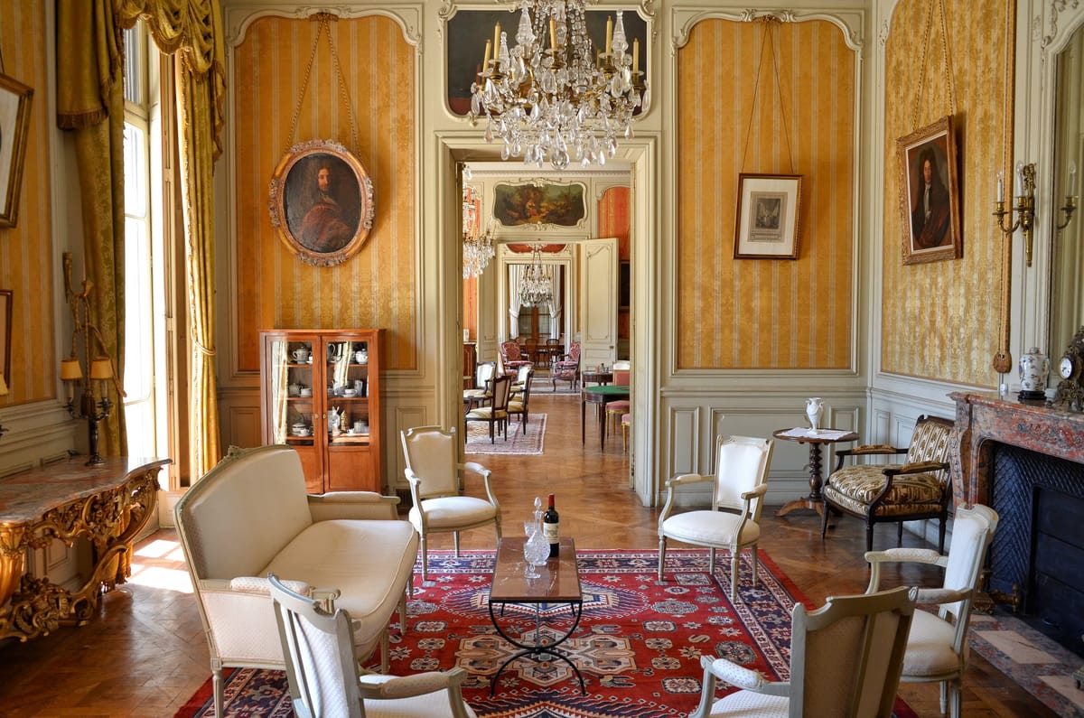 Reception salon at Château du Terral with armchairs, portraits and a marble fireplace