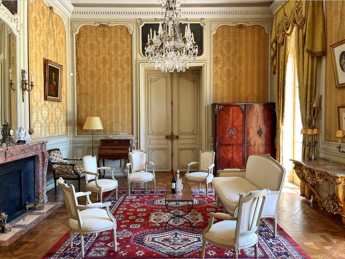 Spacious salon at Château du Terral with cream armchairs, red rug and double doors