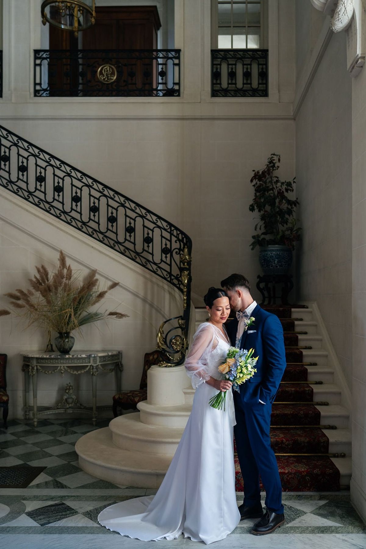Couple embrace by the wrought-iron staircase and carpeted steps in Château du Terral's entrance hall